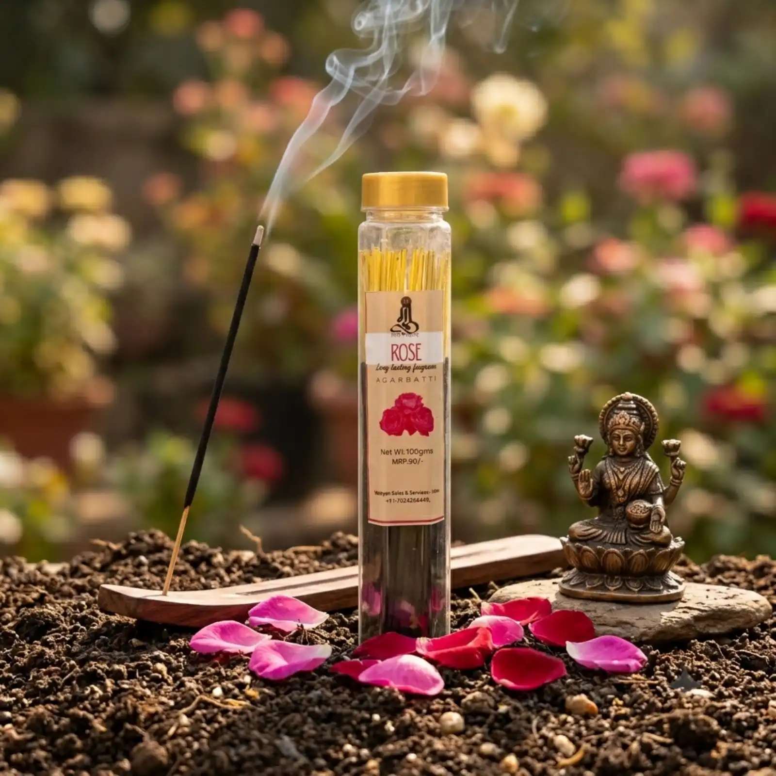GURU Rose Agarbatti jar outdoors on soil with red rose petals and a brass Lakshmi idol